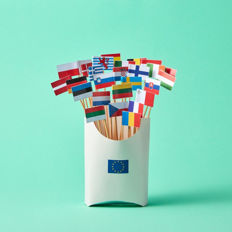 Set of different paper flags in cardboard box decorated with EU sign on green background with copy space. Economic, Political Union of European States
